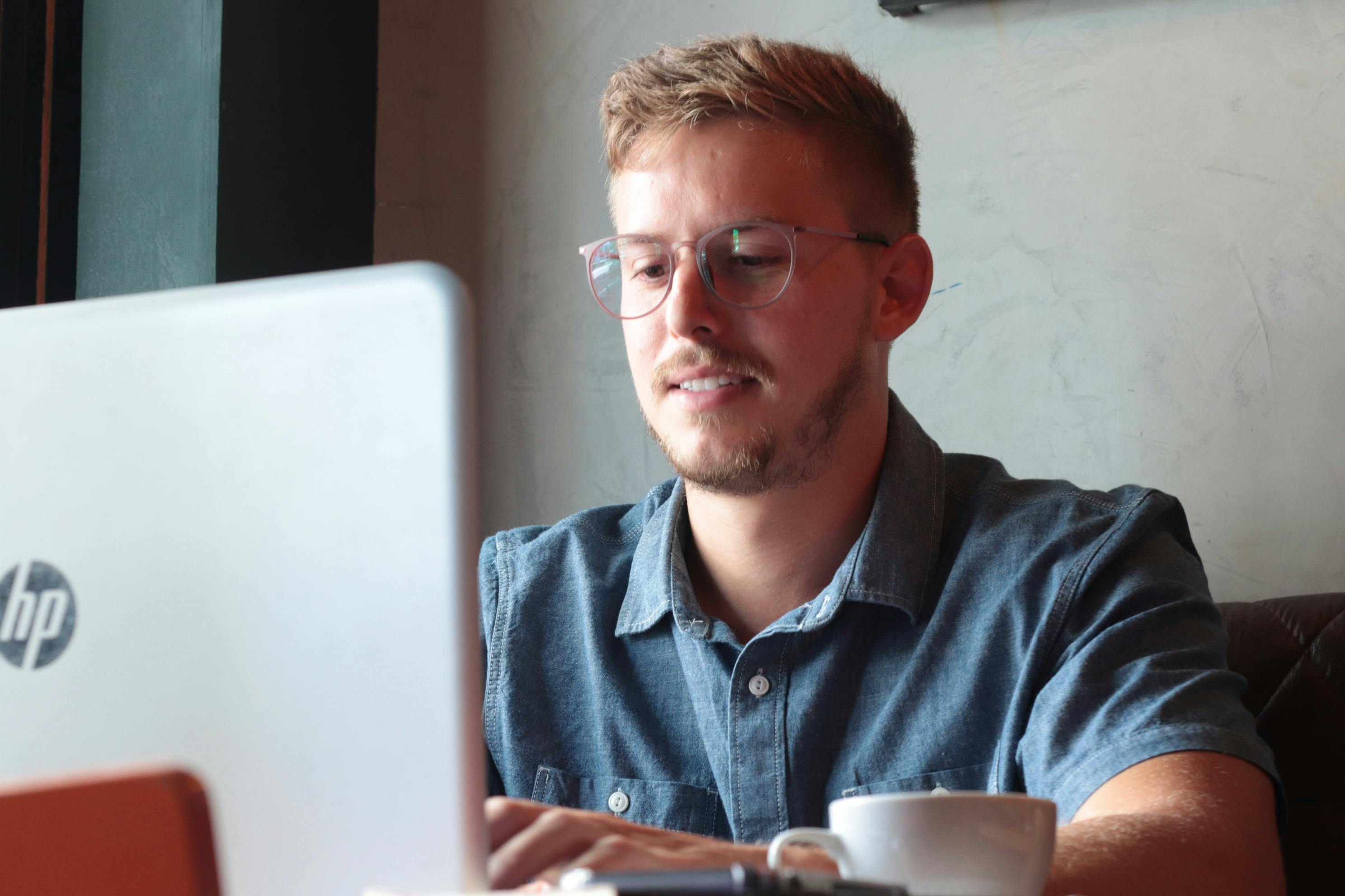 A man in glasses working on a laptop in a coffee shop
