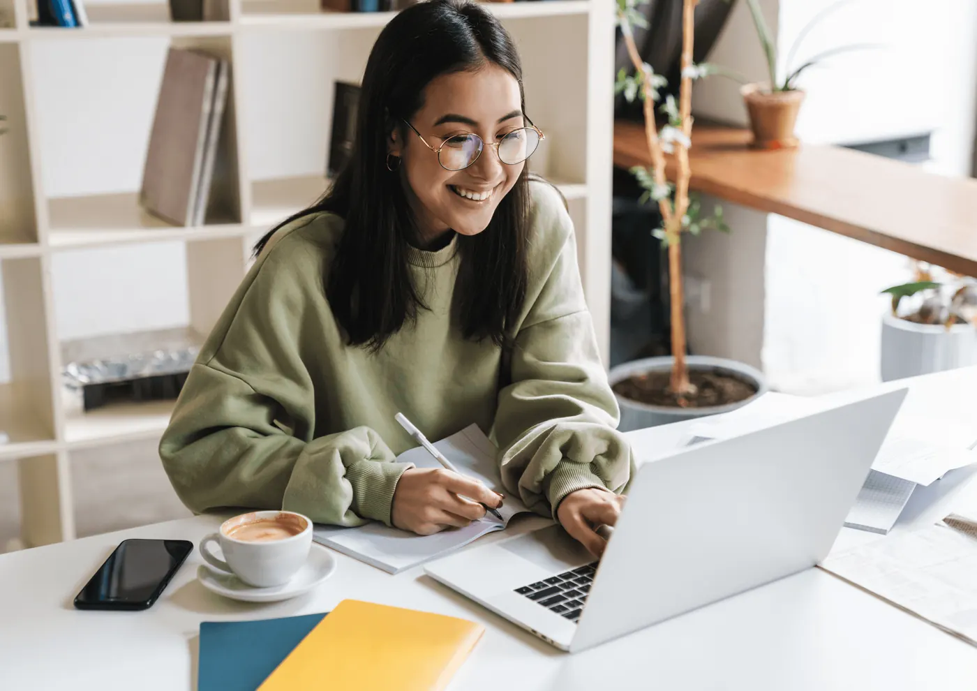 A designer smiling and taking notes in front of her laptop