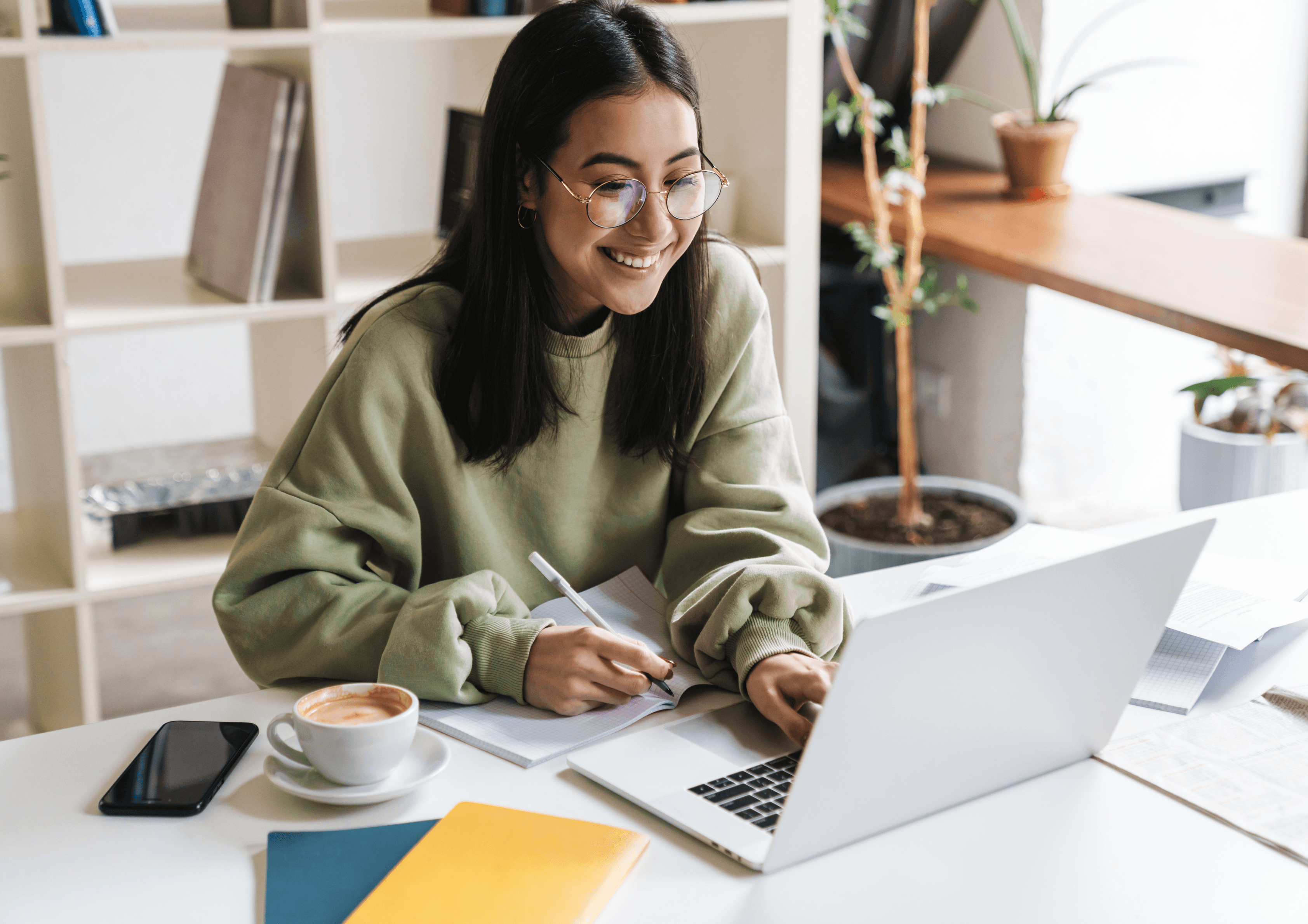 A designer smiling and taking notes in front of her laptop