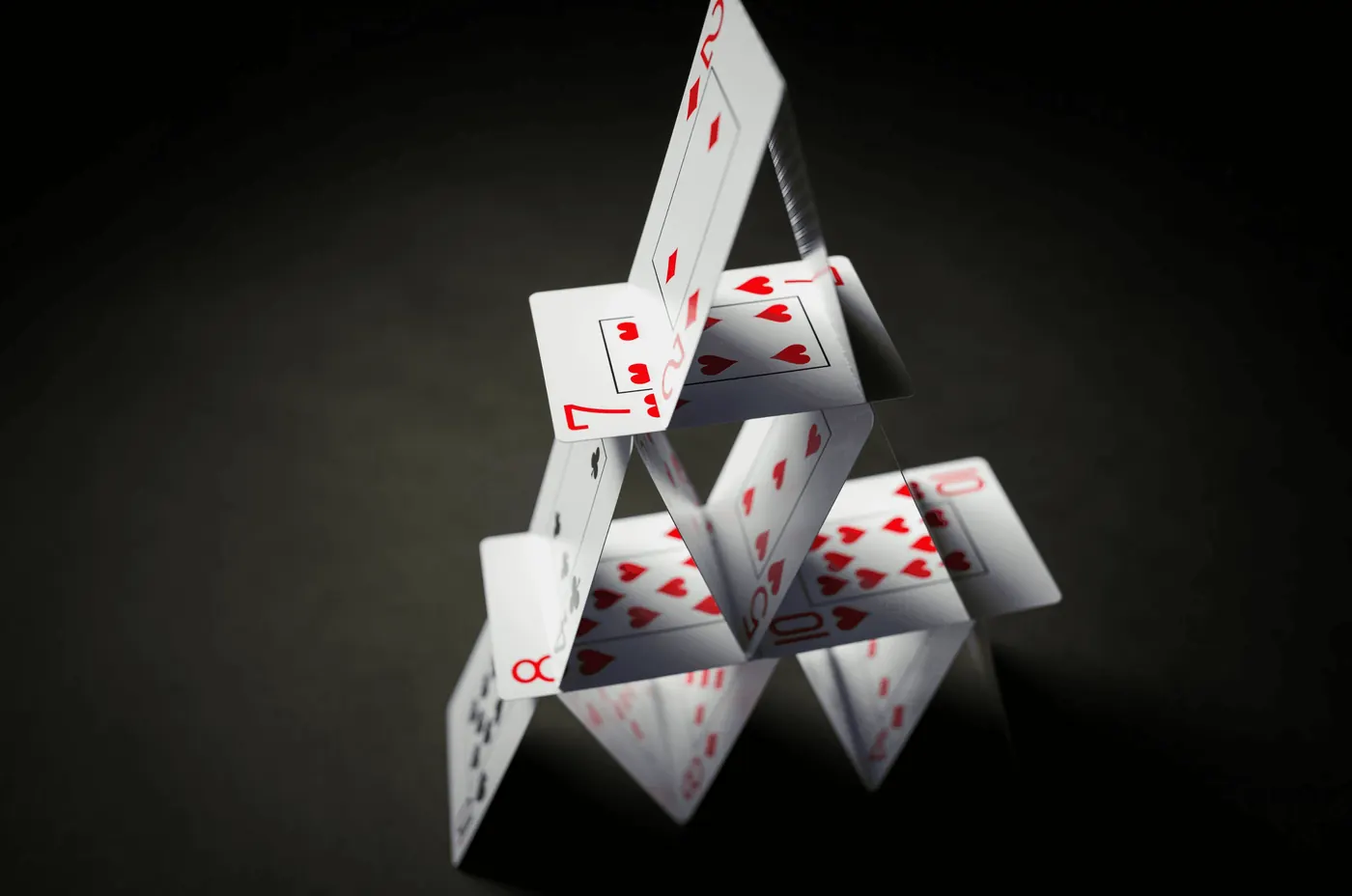 A house of playing cards balanced on a dark table, one nudge from collapse